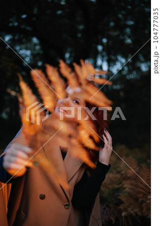 Young woman hiding behind fern leaf in dark forest 104777035