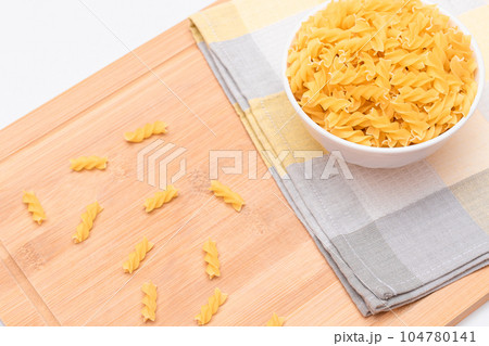 Uncooked Fusilli Pasta in White Bowl on Wooden Board 104780141