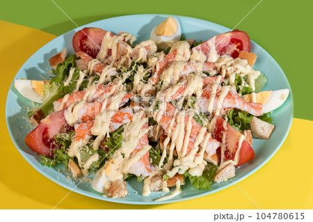 Salad with lettuce, chicken, cherry tomatoes and eggs. Seasoned with sauce. On a colored background. Salad with lettuce, chicken, cherry tomatoes and eggs. Seasoned with sauce. On a colored background. 104780615