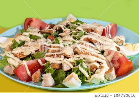 Salad with lettuce, chicken, cherry tomatoes and eggs. Seasoned with sauce. On a colored background. 104780616