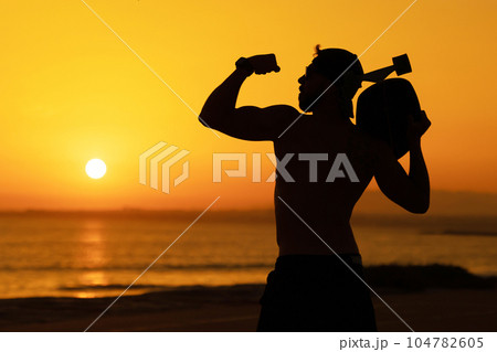 Silhouette of a fit man showing biceps against the background of a bright sunset 104782605