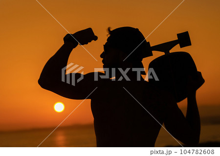 Silhouette of a pumped-up man showing biceps against the background of a bright sunset Silhouette of a pumped-up man showing biceps against the background of a bright sunset 104782608
