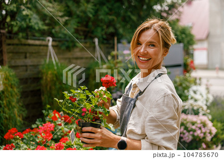 Smiling woman florist business owner standing with houseplant on background of floral store  104785670