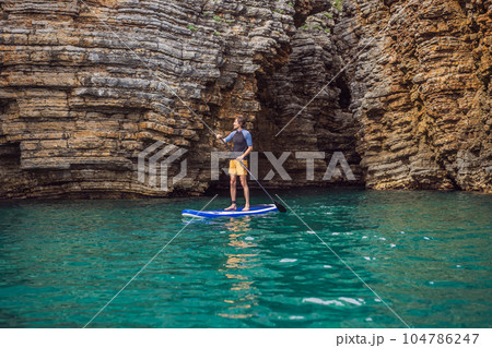 Young men Having Fun Stand Up Paddling in blue water seaamong the rocks in Montenegro. SUP 104786247