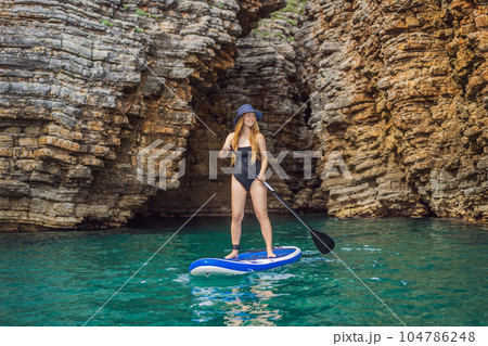 Young women Having Fun Stand Up Paddling in blue water seaamong the rocks in Montenegro. SUP 104786248