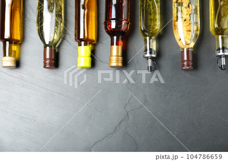 Different sorts of cooking oil in bottles on grey table, flat lay. Space for text Different sorts of cooking oil in bottles on grey table, flat lay. Space for text 104786659