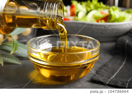 Pouring cooking oil into bowl on grey table, closeup 104786664
