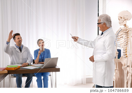 Medical students and professor studying human skeleton anatomy in classroom 104786689