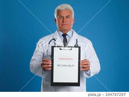 Doctor holding clipboard with words HEMORRHOID WE CAN HELP on blue background 104787207