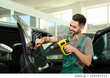Worker tinting car window with heat gun in workshop Worker tinting car window with heat gun in workshop 104787213