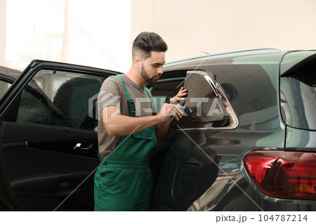 Worker tinting car window with foil in workshop Worker tinting car window with foil in workshop 104787214
