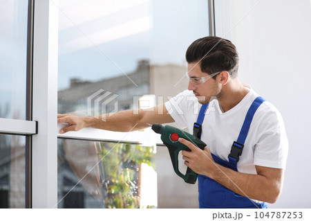 Construction worker repairing plastic window with electric screwdriver indoors Construction worker repairing plastic window with electric screwdriver indoors 104787253