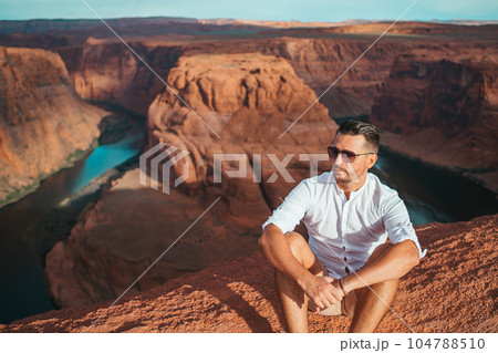 Happy man on the edge of the cliff. Horseshoe Bend Canyon in Page, Arizona. Adventure and tourism concept Happy man on the edge of the cliff. Horseshoe Bend Canyon in Page, Arizona. Adventure and tourism concept 104788510