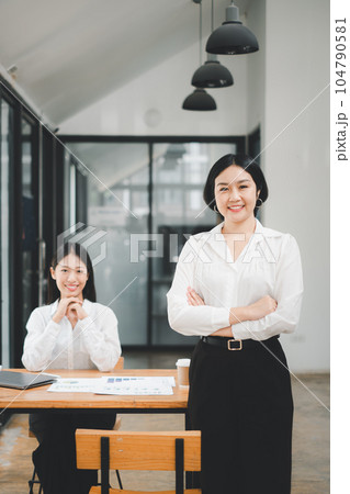 Happy business woman standing competently and smiling in open plan office with blurry collea gues sitting in office as background, Business concept. Happy business woman standing competently and smiling in open plan office with blurry collea gues sitting in office as background, Business concept. 104790581