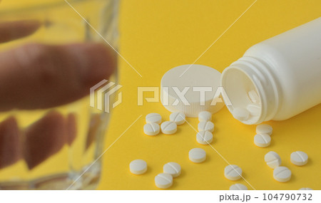 手に持ったコップと白い錠剤と黄色の背景 手に持ったコップと白い錠剤と黄色の背景 104790732