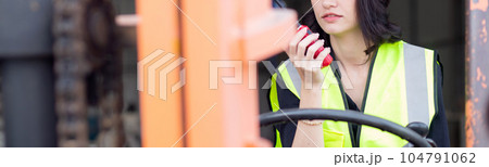 Young asian woman is foreman using radio for communication while driving forklift. 104791062