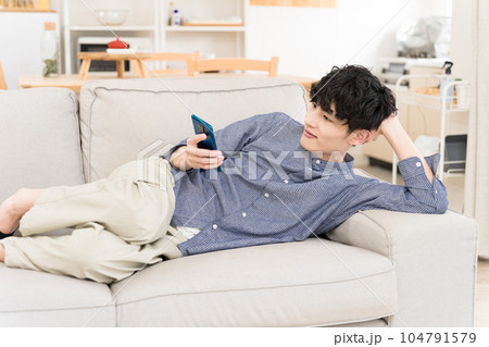 ソファーに寝そべってスマホを見ている若い男性 ソファーに寝そべってスマホを見ている若い男性 104791579