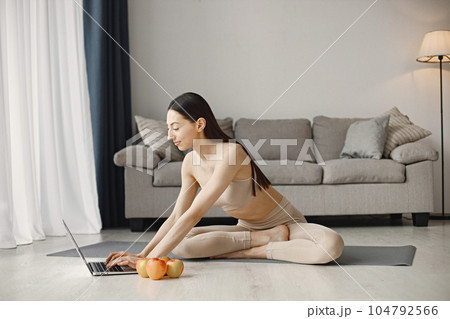 Slim and beautiful woman wearing beige leggins and top and sitting on yoga mat. Young girl with fit body posing at home with fresh apples. Sport, fitness, diet, nutrition and health care concept. Slim and beautiful woman wearing beige leggins and top and sitting on yoga mat. Young girl with fit body posing at home with fresh apples. Sport, fitness, diet, nutrition and health care concept. 104792566