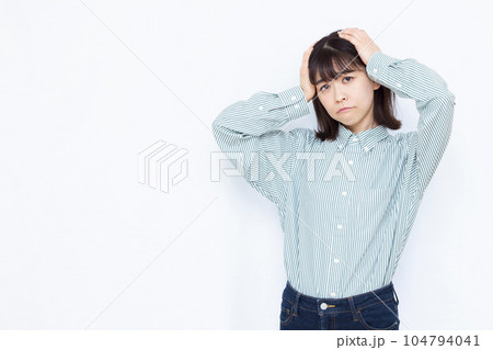 白い背景の前で頭を抱えて悩む30代の女性 白い背景の前で頭を抱えて悩む30代の女性 104794041
