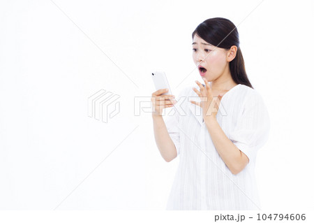 白い背景の前でスマホを持ちビックリしている30代の女性 白い背景の前でスマホを持ちビックリしている30代の女性 104794606