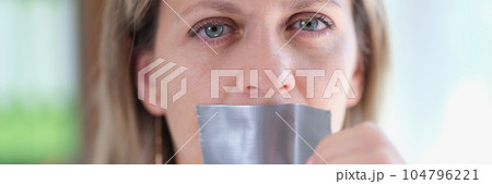 Young woman unsticking duct tape on mouth Young woman unsticking duct tape on mouth 104796221