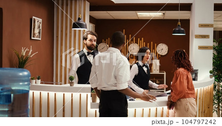 Tracking shot of african american tourists wanting to upgrade hotel stay, talking with helpful hotel personnel. Guests requesting extra room amenities not included in holiday package deal 104797242
