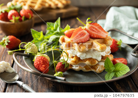 Homemade Belgian waffles with fresh berrie strawberries and ricotta cheese for breakfast on a rustic table. Homemade Belgian waffles with fresh berrie strawberries and ricotta cheese for breakfast on a rustic table. 104797635