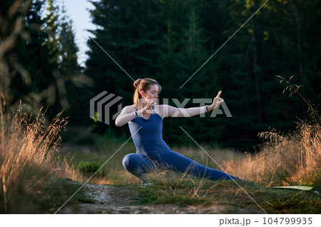 Sporty woman practicing yoga in forest. Middle-aged woman exercising early in morning. Female doing sport outdoor. Sporty woman practicing yoga in forest. Middle-aged woman exercising early in morning. Female doing sport outdoor. 104799935