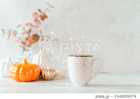 Details of Still life, cup of tea or coffee, pumpkins, candle, brunch with leaves on white table background, home decor in a cozy house. Autumn weekend concept. Fallen leaves and home decoration. Details of Still life, cup of tea or coffee, pumpkins, candle, brunch with leaves on white table background, home decor in a cozy house. Autumn weekend concept. Fallen leaves and home decoration. 104800074