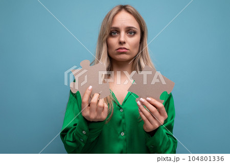 worried young blond woman holding a puzzle in her hands on a blue background 104801336