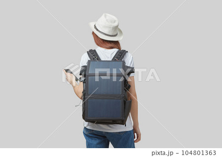 Girl carrying backpack with flexible solar panel attached to smartphone in her hands, isolated on light gray 104801363