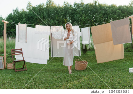 Laundry day. A woman hangs linen and towels on a tree in the courtyard of a village house. Laundry day. A woman hangs linen and towels on a tree in the courtyard of a village house. 104802683