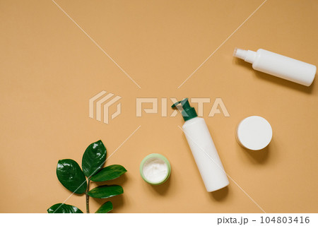 Set of organic SPA cosmetics with green leaves. Top view of bottles made of white recyclable plastic on a beige sand background with a copy space. Packaging design of natural cosmetic products for Set of organic SPA cosmetics with green leaves. Top view of bottles made of white recyclable plastic on a beige sand background with a copy space. Packaging design of natural cosmetic products for 104803416