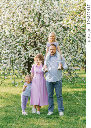 Young family with two girls and daughters on the background of a blooming garden Young family with two girls and daughters on the background of a blooming garden 104803417