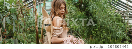 A beautiful young woman takes care of plants in a greenhouse. The concept of gardening and an eco-friendly lifestyle. 104803442