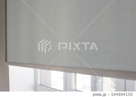 Details of gray fabric roller blinds. Automatic curtain close-up on the window. Selective focus. Motorized shades. City outside the window. Details of gray fabric roller blinds. Automatic curtain close-up on the window. Selective focus. Motorized shades. City outside the window. 104804150