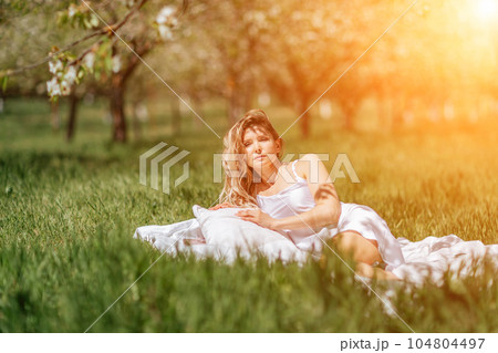 woman garden. she sleeps on a white bed in the fresh spring grass in the garden. Dressed in a blue nightgown. woman garden. she sleeps on a white bed in the fresh spring grass in the garden. Dressed in a blue nightgown. 104804497