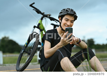 Smiling asian man cyclist taking a break resting from cycling bike in the morning and using mobile phone 104804970
