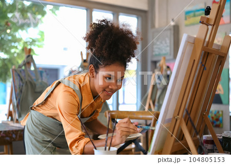 Talented African American female artist creating masterpiece, painting picture with brush on canvas in art studio 104805153