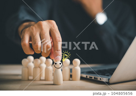 A happy wooden person figure holds a light bulb, embodying creative thinking and inspiration. Leadership and teamwork create an environment where ideas are shared and new concepts are born. 104805656