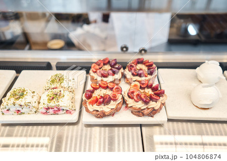 A variety of cakes covered with chocolate and decorated with pistachio mousse. A showcase in a pastry shop with delicious desserts with fresh berries and cream. Delicious pastries in the coffee shop. 104806874