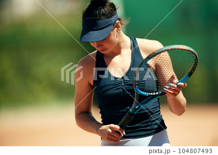 Portrait of young woman, tennis player in sportswear standing with racket. Outdoor training at open air tennis court Portrait of young woman, tennis player in sportswear standing with racket. Outdoor training at open air tennis court 104807493
