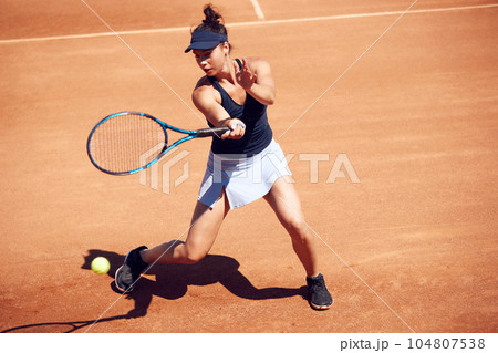 Yng sportive woman, professional athlete training,. playing tennis outdoors at open air stadium on warm sunny day Yng sportive woman, professional athlete training,. playing tennis outdoors at open air stadium on warm sunny day 104807538