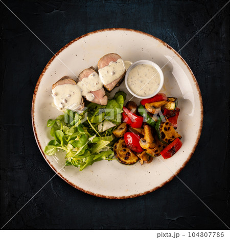 Sliced pork medallions surrounded with roasted vegetables 104807786