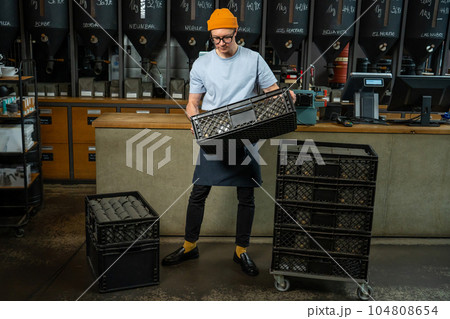 Male worker or business owner uploads packages of coffee on factory or warehouse. 104808654