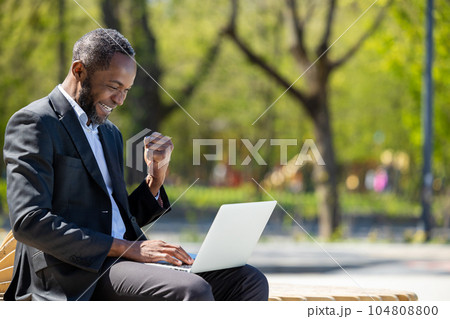 African american businessman working on laptop in the park and looking contented African american businessman working on laptop in the park and looking contented 104808800