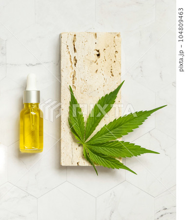 Dropper bottle with pipette near green cannabis leaves and stone top view on marble. CBD oil Dropper bottle with pipette near green cannabis leaves and stone top view on marble. CBD oil 104809463