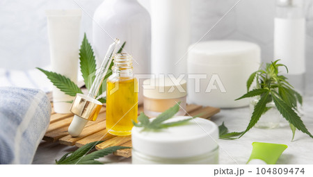 Dropper bottle with CBD oil and cream bottles green cannabis leaves close up Dropper bottle with CBD oil and cream bottles green cannabis leaves close up 104809474