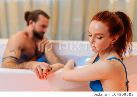 Close-up of cute young woman in bikini and handsome bearded man sitting in double hot bath tub with hydromassage at luxury spa salon, enjoying weekend in bathtub. Concept of romantic relationship. 104809985