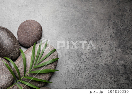 Spa stones and palm leaf on grey table, flat lay. Space for text 104810350